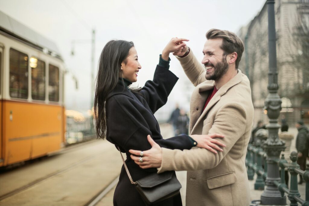 Home Joyful couple dances on a tram-lined city street, sharing laughter and happiness.