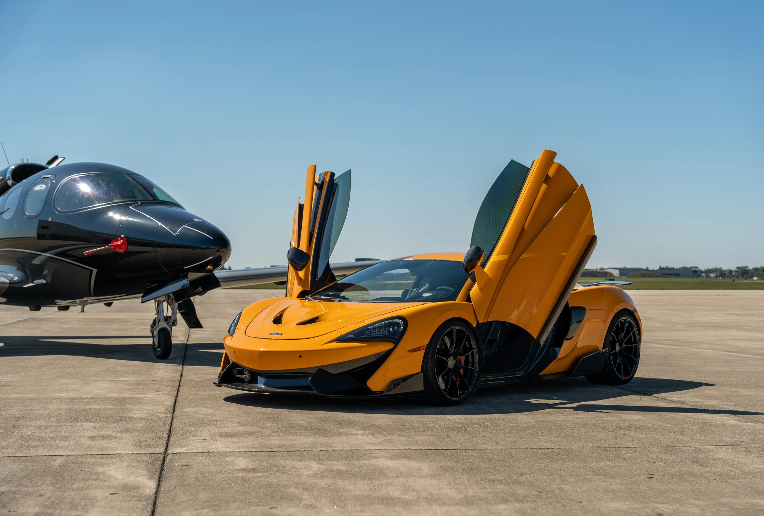 A striking scene of a luxury sports car with butterfly doors open beside a sleek private jet on a clear day.